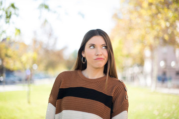 Gloomy, wondering young woman looking up with lips together, being upset thinking about something important, keeps hands down.