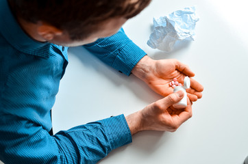 Young businessman in blue shirt holding a jar with a pills at the table at home