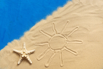 Fototapeta na wymiar Drawn sun on the sea sand and starfish on a blue painted background. Vacation and travel concept. Studio shot.