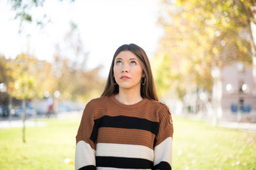 portrait of mysterious charming female with straight hair looking up with enigmatic smile. Beautiful smiling girl looking up standing against gray wall.