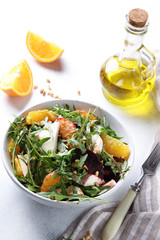 Healthy food. Fresh salad with arugula, mozzarella, baked beetroot, oranges and pine nuts in the bowl with bottle of olive oil and fork. Background image, copy space