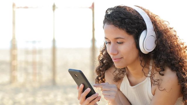 Latin woman listening and feeling music from smart phone outdoors on the beach