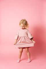 A little girl in a pink dress is spinning and demonstrating her outfit.