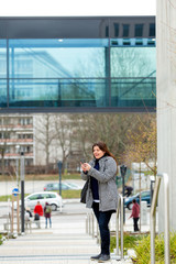 Fototapeta na wymiar Business Woman sends text message on her mobile phone. She is outside the office in a mild winter day.