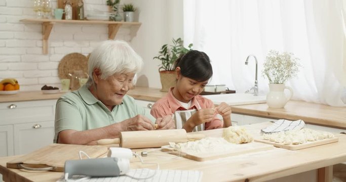 Asian grandmother cooking together with her teen granddaughter, preparing dough for dumplings, spending time together - family ties, concept 4k footage