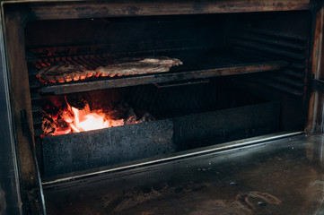 the cook prepares juicy meat steaks in a large oven on a charcoal grill
