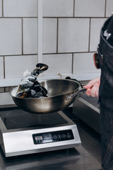 the cook prepares mussels in shells in the kitchen with milk sauce in a large pan