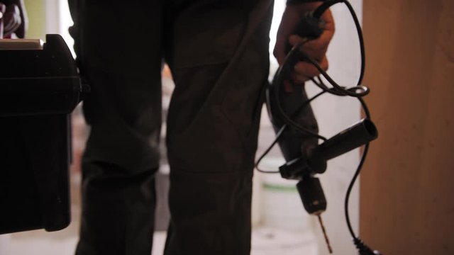 Man in the uniform with drilling machine and toolbox entering the room. Slow-motion follow shot