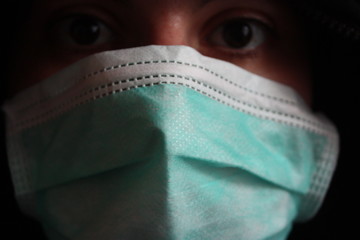 Unrecognizable hooded mysterious individual with dark sweatshirt wears a normal blue surgical mask