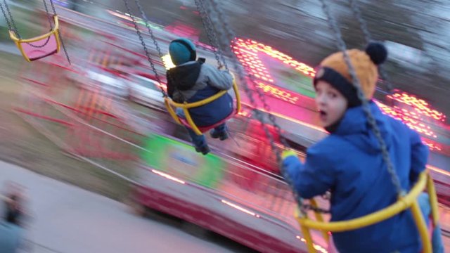 Child, cute boy riding chain swing carousel on sunset, motion blur, colorful background