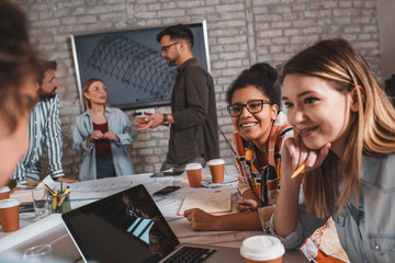 Group of modern business people in casual wear discussing architectural designs while sitting in the creative office.