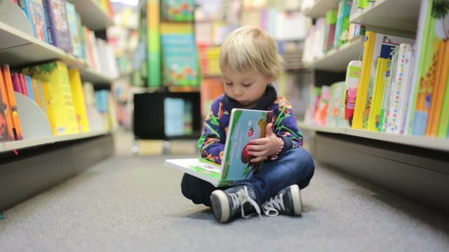 Adorable little boy, sitting in a book store and read book