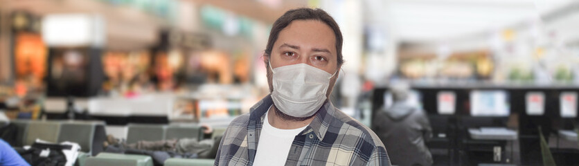 A middle-aged man in a protective mask stands in the airport lounge. The concept is virus protection in public places during travel and tourism.