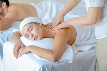 Close up of young woman enjoy with body massage in spa room with day light and the other man lie on bed beside.