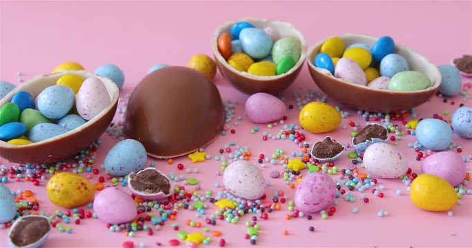 Female Hand Took Easter junk-food, confectionery and unhealthy eating concept - chocolate eggs and drop candies on table. Pink Background