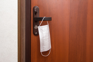 A medical mask hangs on the front door of the apartment. Corona virus protection. Individual respiratory protection.