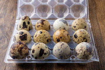 Top view of a dozen quail eggs in plastic packaging, on dark wooden table horizontal