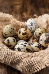 Obraz premium Top view of quail eggs on sackcloth, with selective focus, on dark wooden table in vertical