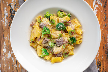 Rigatoni pasta with beef on a white plate with Parmesan and steamed broccoli