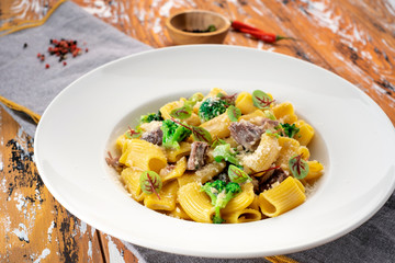 Rigatoni pasta with beef on a white plate with Parmesan and steamed broccoli