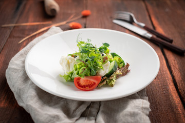 Light diet salad of mozzarella and fresh vegetables -cucumber, tomato, lettuce, peas on a white plate on a wooden background