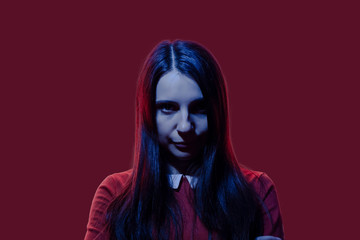 Brunette girl portrait in purple and blue lights. Female in red dress white collar in neon light. mysterious and scary woman face portrait with color flashes. witch in red and blue lighting