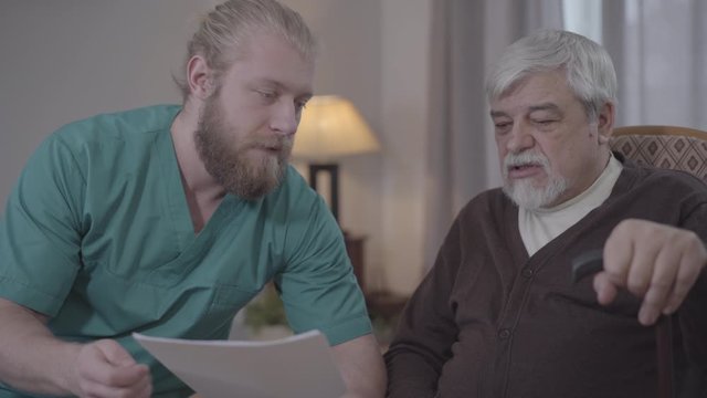 Close-up of Caucasian male nurse explaining matter of documents to mature retiree. Man assisting senior in nursing home. Help, support, aging, lifestyle.