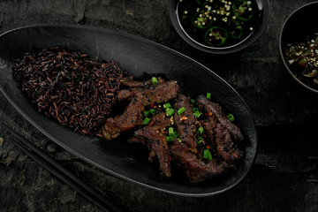 Chinese black pepper beef stir fry with black rice in a black clay plate on an old rustic table. Directly above top view shot.