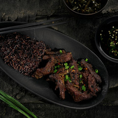 Delicious sticky Asian beef meat in black pepper sauce with black rice on a rustic wooden black table. Directly above top view shot.