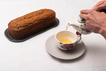 Hand spilling tea in a cup with a Carrot cake freshly brewed for breakfast