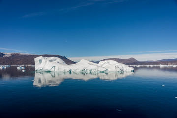 Iceberg in Greenland fjord with reflection in calm water. Sunny weather. Golden hour.