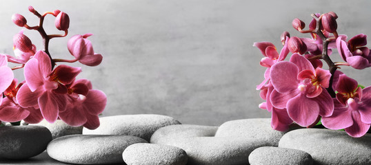 Composition with spa stones, orchid pink flower on grey background.