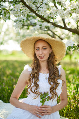 The beautiful girl the blonde in the blossoming apple-trees garden. White flowers in a garden in sunshine. Spring apple trees in blossom. Beautiful woman among spring blossom