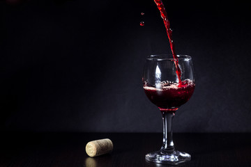 Red wine pouring from the bottle to the glass with splashes on black background