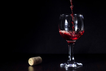 Red wine pouring from the bottle to the glass with splashes on black background