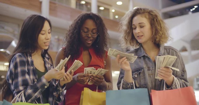 Happy young women with shopping bags and cash in mall