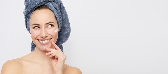 Beautyful woman with perfect skin and cream on her cheek smiling and looking at copy space 