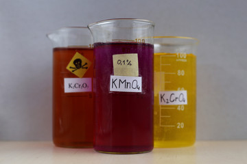 A 100-milliliter beaker filled with a purple aqueous solution of potassium permanganate, against the background of other colored solutions of chromium salts.