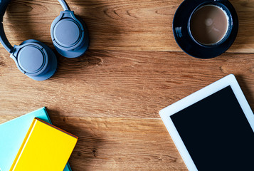 Composition of digital tablet notebooks headphones and coffee on a desk with wooden background