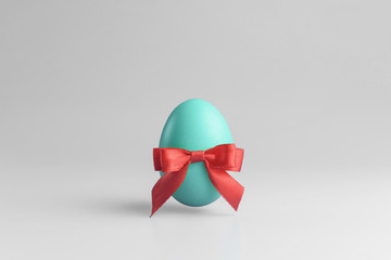 One blue egg  with a red ribbon bow on a white background. Minimal Happy Easter concept decoration. Copy space for text mockup.