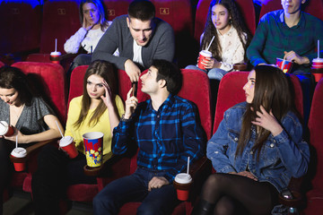 Fototapeta premium A man is talking loudly on the phone in a movie theater and prevents you from watching a movie. The man makes a remark and asks to turn off the phone.