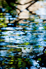 Small paper boat floating in the colorful water of the pond. Message of serenity and calm 1
