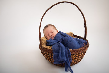 New born baby wrapped in blue cloth laying asleep in basket on solid background 