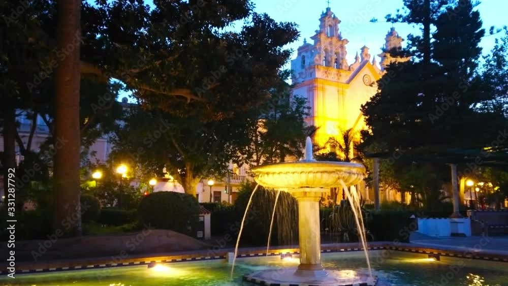 Canvas Prints The evening in Alameda Marques de Comillas garden with a view on vintage stone fountain and illuminated Carmen Church on background, Cadiz, Spain