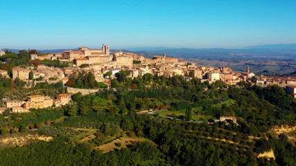 Fototapeta na wymiar Drone flying over a magnificent authentic Italian cityscape and green meadows. Aerial view of the beautiful medieval old town of Montepulciano with red roofs Tuscany, Italy