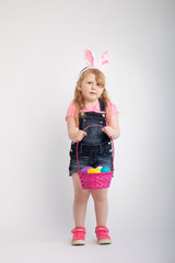 Young blonde girl wearing white easter bunny ears holding pink holiday easter basket filled with colorful plastic Easter eggs 