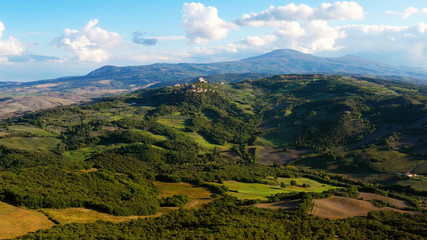 Drone flying over a magnificent authentic Italian village and green meadows. Aerial view of the beautiful  old village of rocca d'orcia Tuscany, Italy