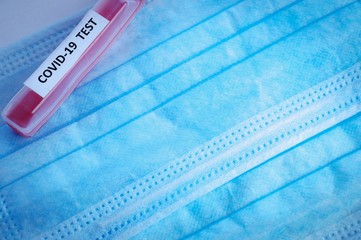 Test tube with the inscription COVID-19 on a background of blue medical masks. The problem of the...