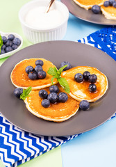 Pancakes served with fresh blueberries on gray plate over geometrical background. Healthy home made breakfast concept
