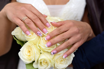 Obraz na płótnie Canvas Hands of the bride with ring on a bouquet of white roses